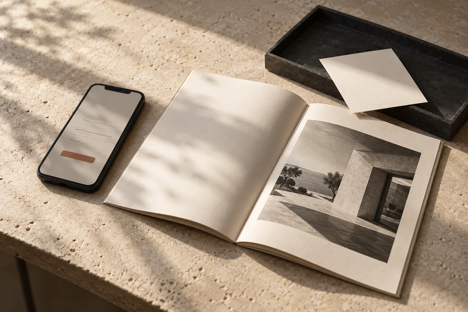Editorial still life of a phone with a simple form beside an open cream brochure and a charcoal tray holding an enquiry card